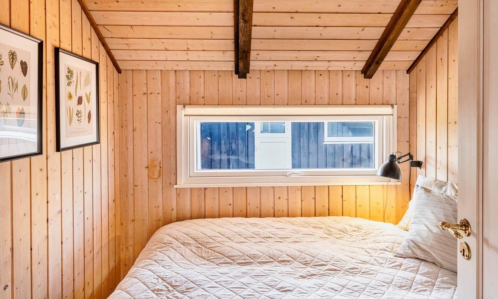 Schlafzimmer mit Holzwandverkleidung, Bett und Fenster. An der Wand hängen zwei Bilder.