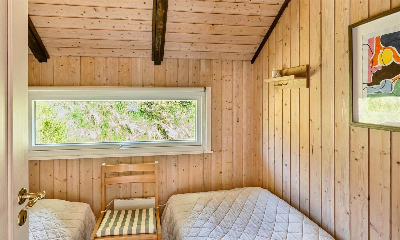 Zimmer mit Holzwand, Bett, Stuhl und Fenster zur grünen Landschaft.