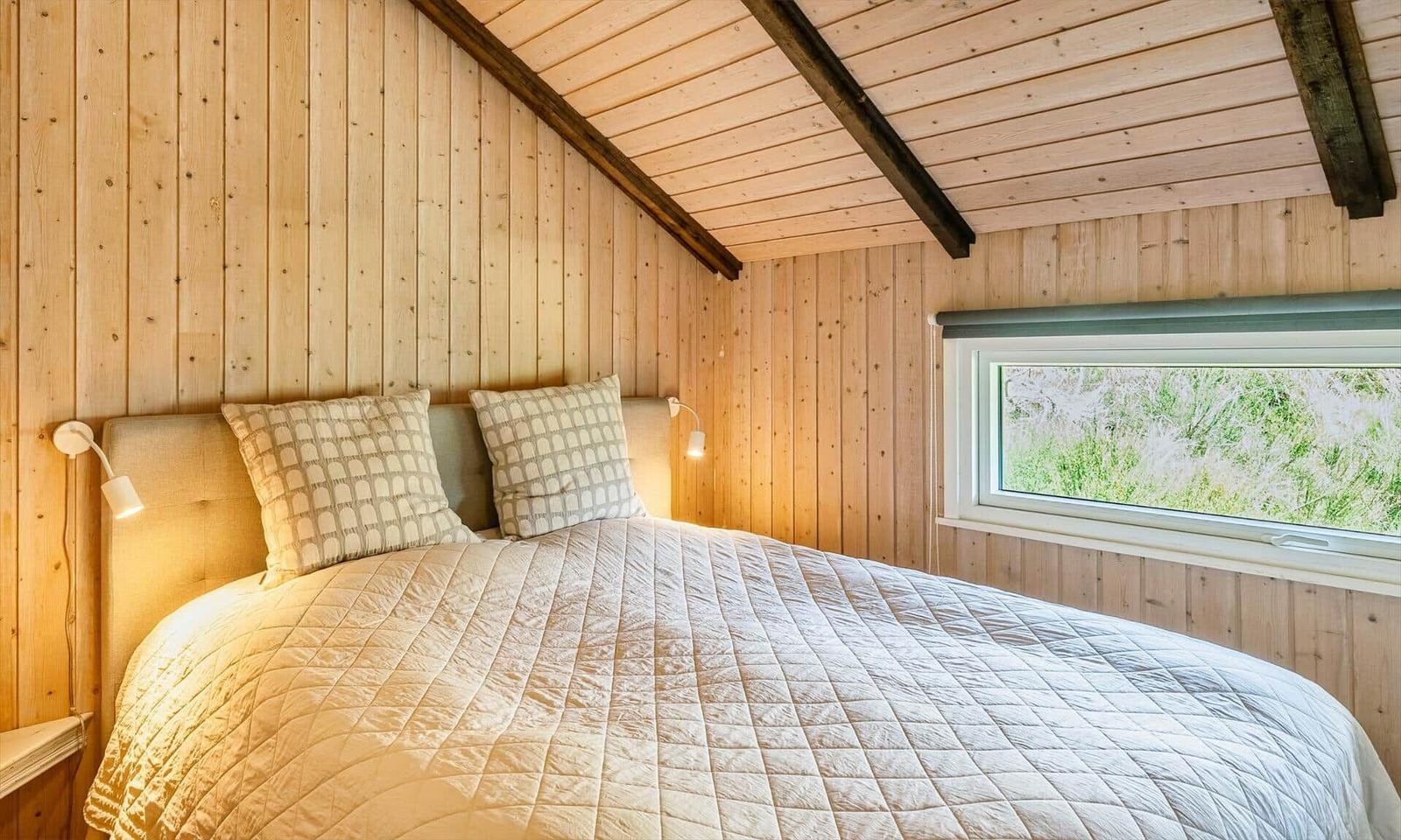Schlafzimmer mit Bett, Fenster und Holzwandverkleidung.