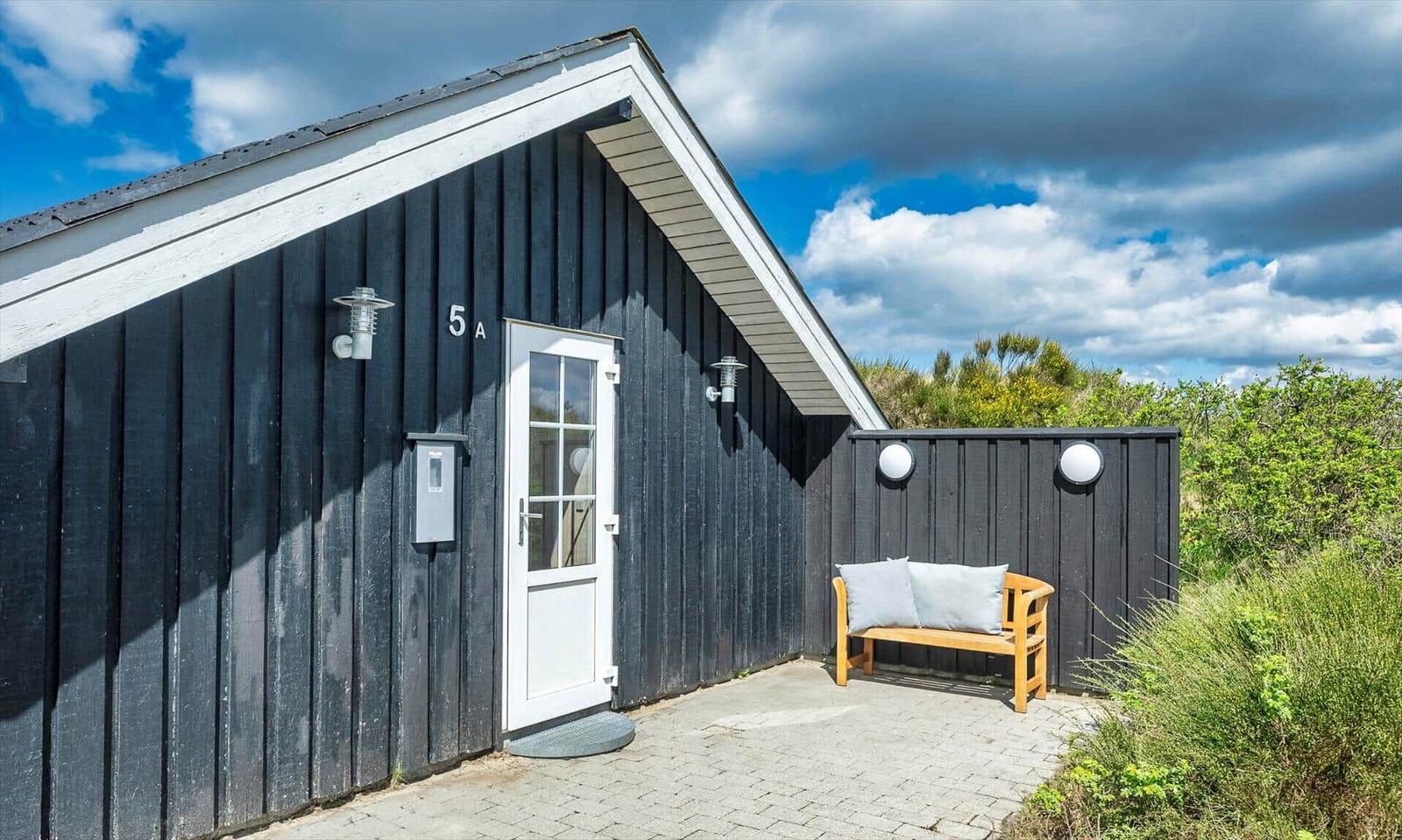 Schwarze Holzhütte mit weißer Tür und Bänke auf gepflastertem Hof