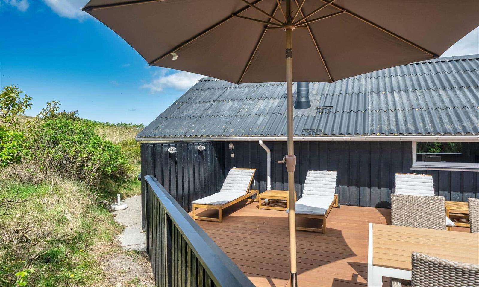 Terrasse mit Liegestühlen und Sonnenschirm neben einem Holzhaus.