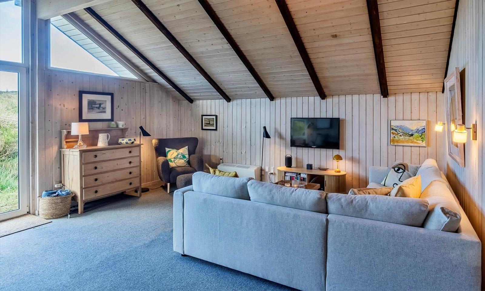 Wohnzimmer mit Sofa, Fernseher und Holzwandverkleidung unter schrägen Dachbalken.