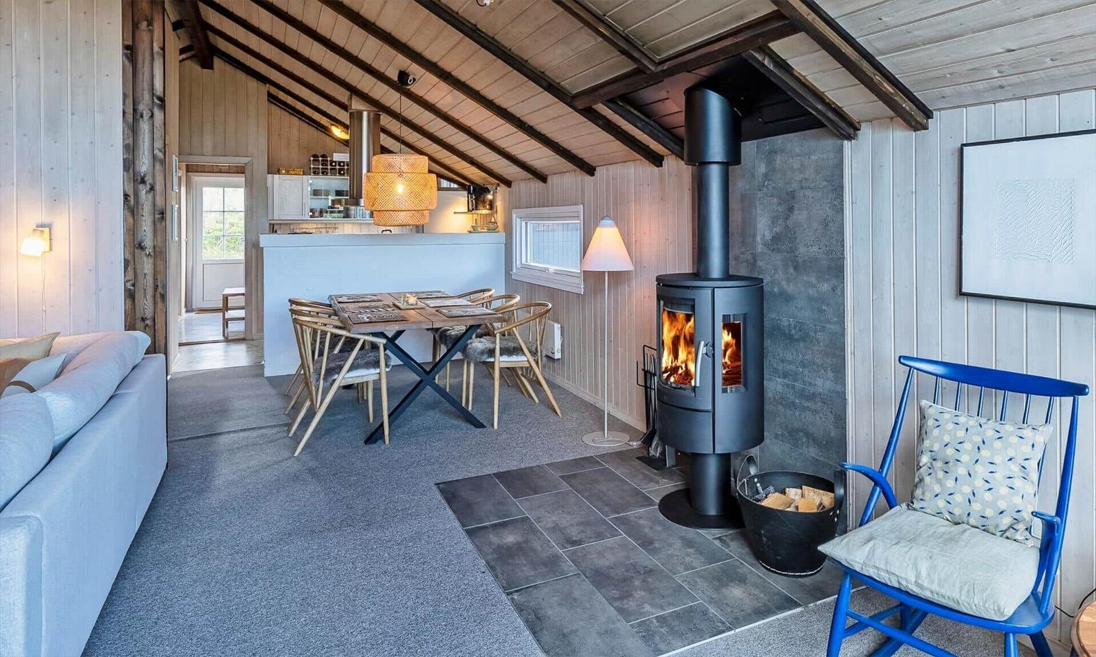 Wohnraum mit Kaminofen, Esstisch und Sofa. Holzdecke und Wandverkleidung.