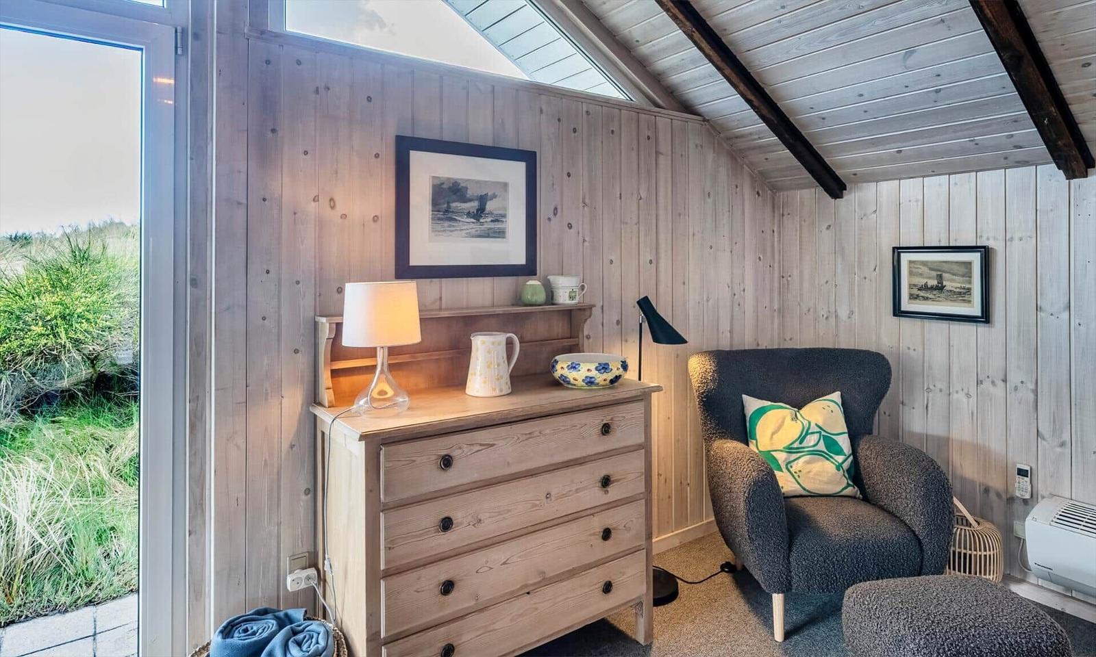 Ein Raum mit Holzwand und Schrank, Sessel und Blick auf Grünflächen.