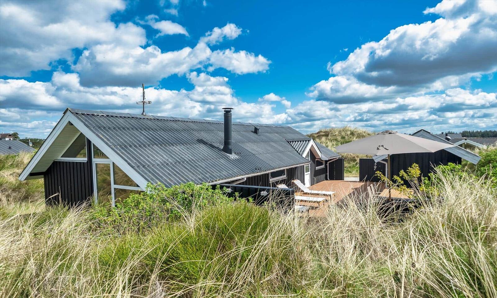 Holzhaus mit Dachterrasse und Sonnenschirm zwischen Gras und Himmel.