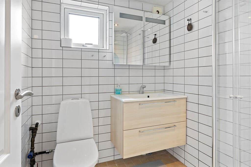 Badezimmer mit Toilette, Waschbecken und Dusche. Wandfliesen und Spiegelschrank.