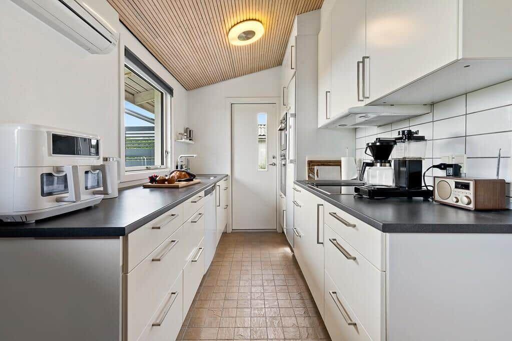 Moderne Küche mit weißen Schränken, dunklem Arbeitsplatz und Holzdecke.