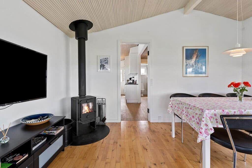 Wohn- und Essbereich mit Holzboden, Kaminofen und Tisch mit Tischdecke.