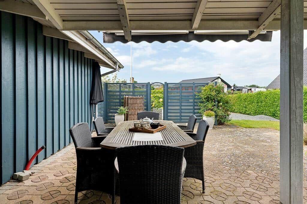 Terrasse mit Tisch und Stühlen unter Dach, Blick auf Garten und Zaun.