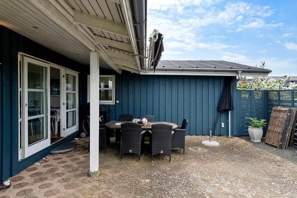 Terrasse mit Tisch und Stühlen unter Dach. Hinterhof mit Zaun und Pflanze.