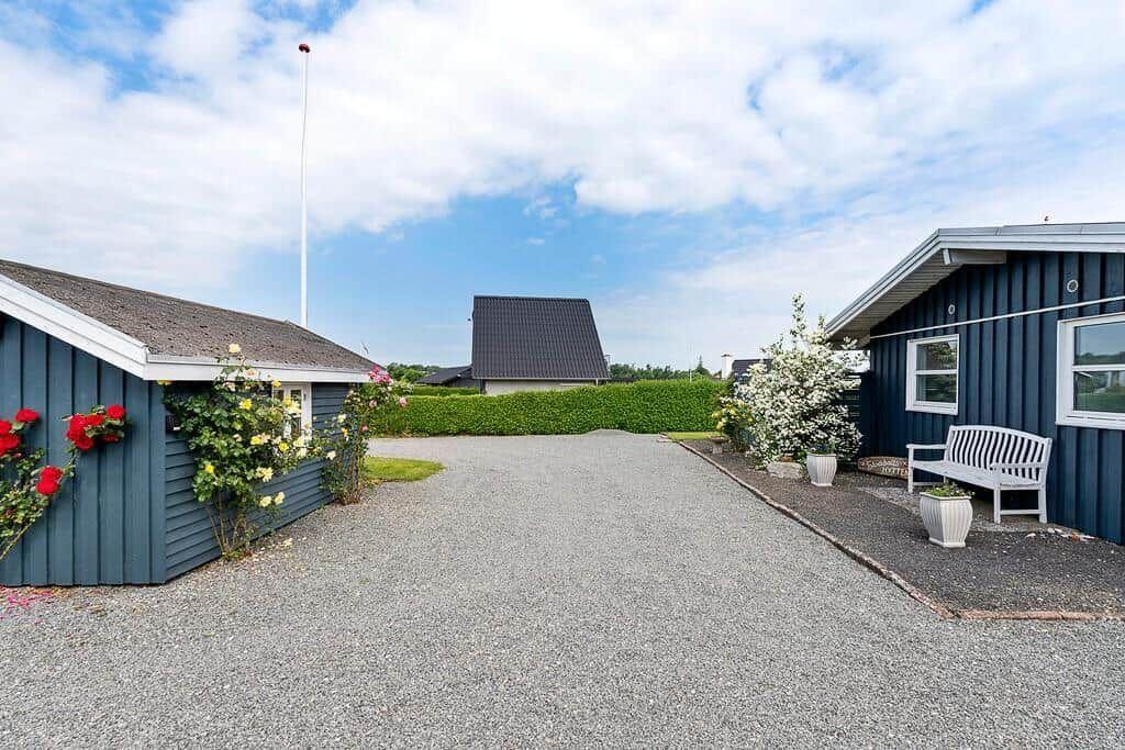 Grauer Kiesweg führt zwischen blauen Gebäuden mit Blumen und einer Bank.