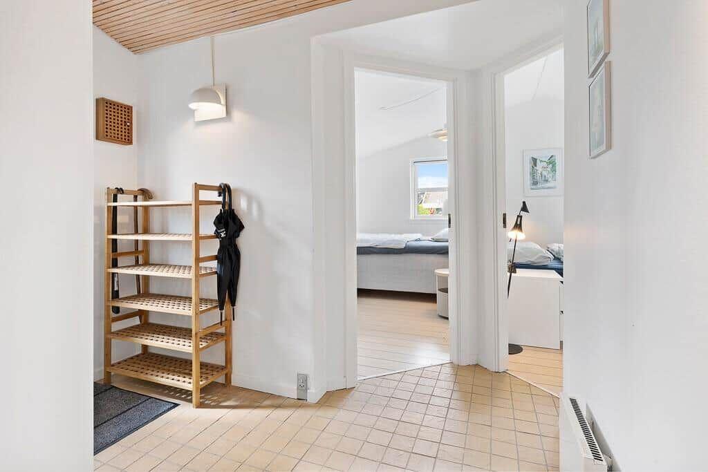 Eingangsbereich mit Holzregal und Blick in Schlafzimmer mit Bett und Fenster.