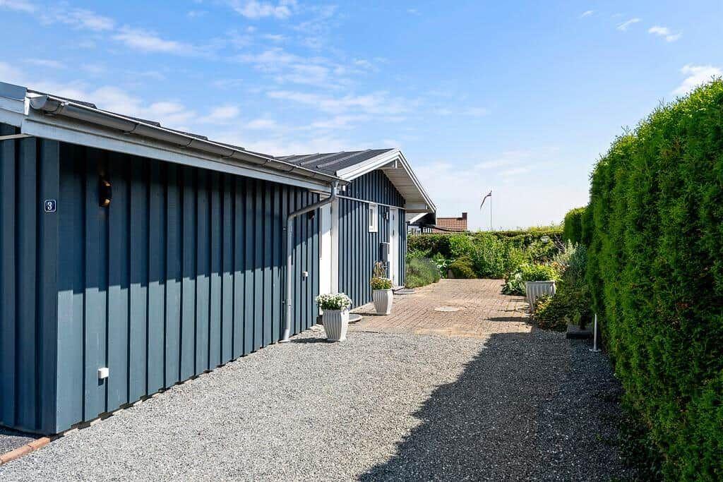Ein graues Ferienhaus mit gepflastertem Weg und grüner Hecke. Nummer 3 an der Wand.