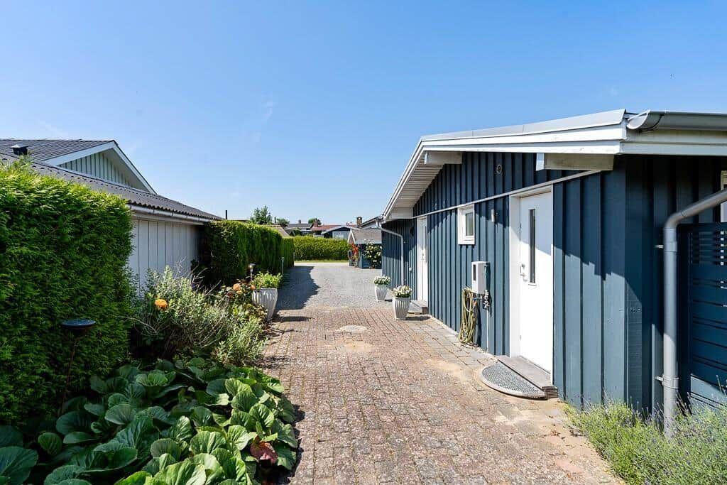 Gartenweg mit blauem Holzhaus und gepflastertem Weg. Grüne Hecken und Blumenbeete flankieren den Pfad.