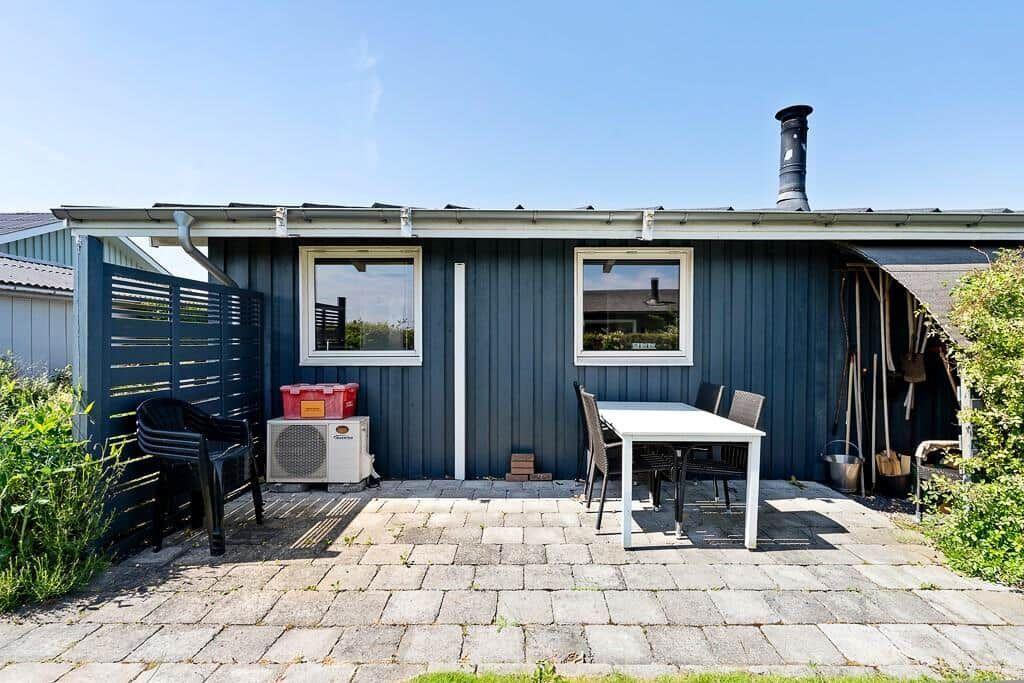 Blauer Holzhaus mit Terrasse, Tisch, Stühlen und Grillbereich.