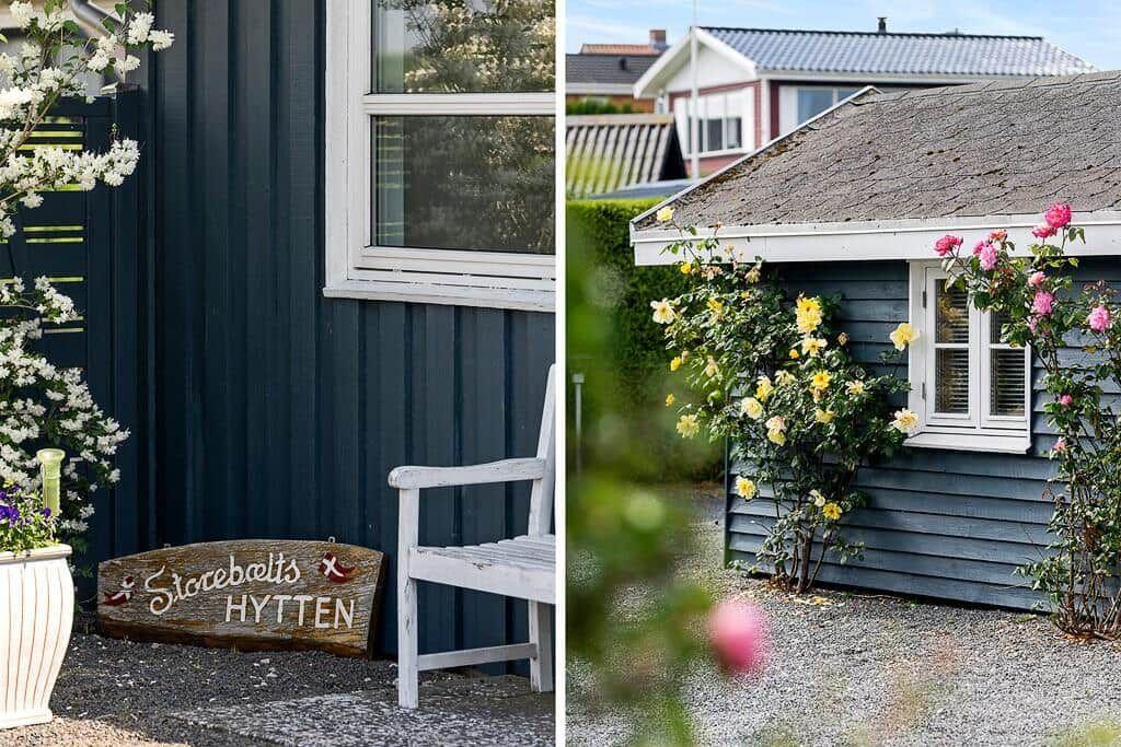 Holztafel mit Schrift, weiße Bank und blühende Rosen an einem blauen Haus