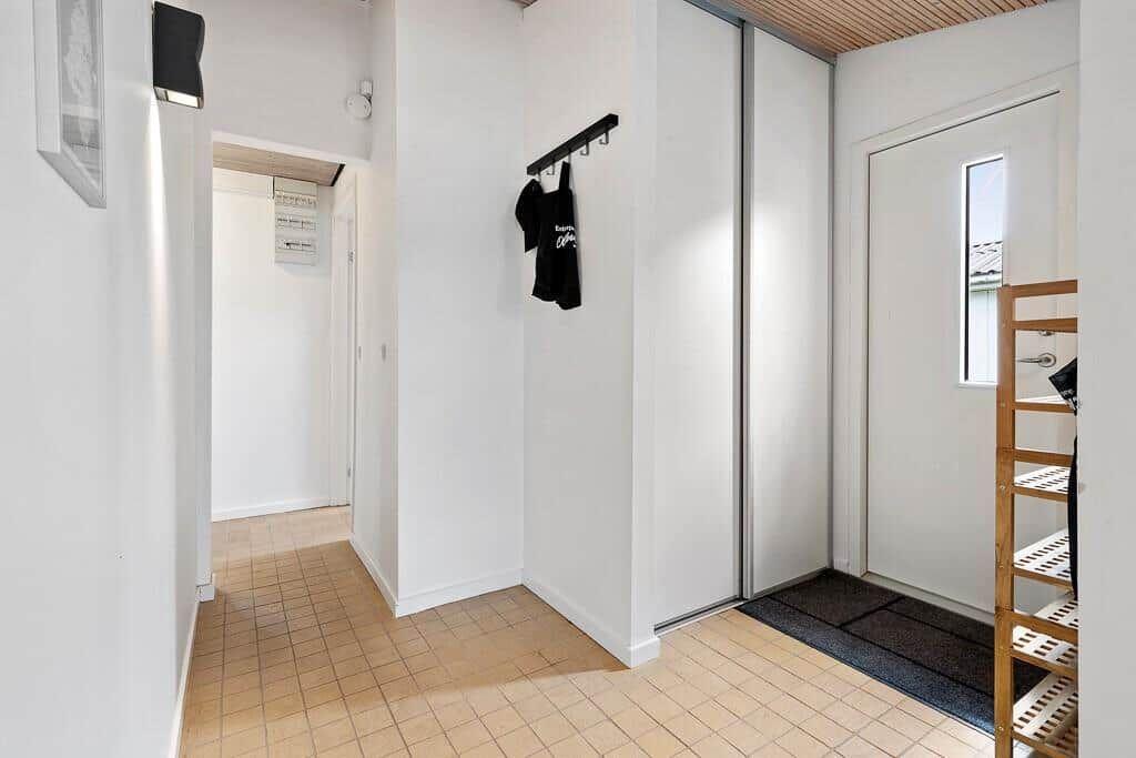 Eingangsbereich mit Schiebetüren, Kleiderhaken und Holzregal. Fliesenboden und weiße Wände.
