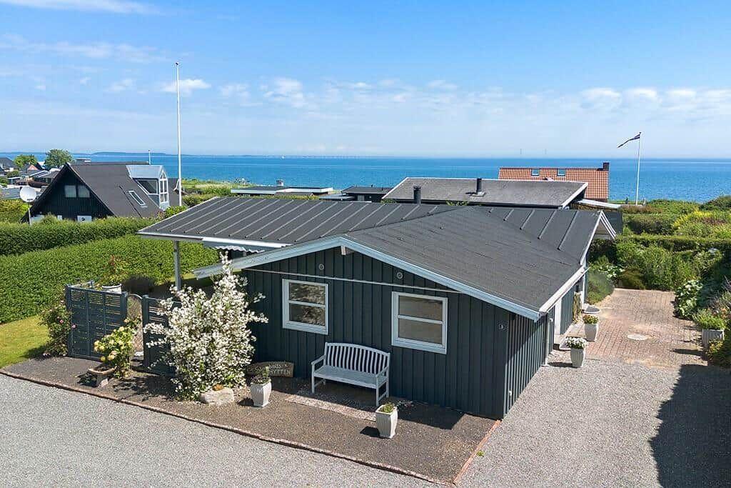 Ein dunkelgrauer Holzhaus mit Blick auf das Meer und einen gepflasterten Hof.