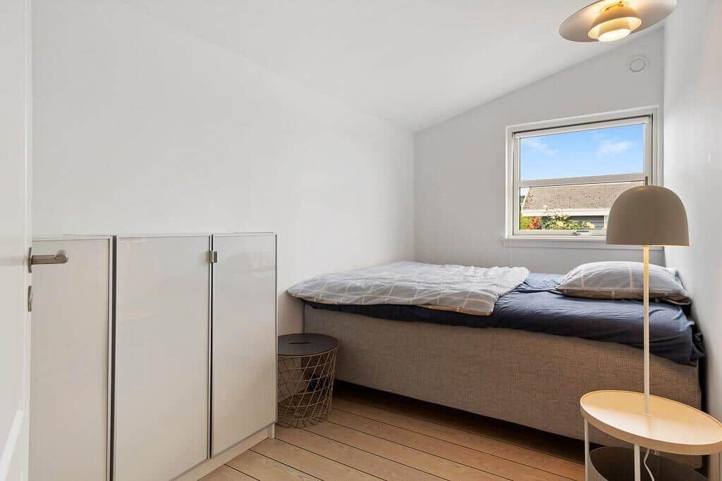 Schlafzimmer mit Bett, Kleiderschrank und Fenster. Holzboden und Stehlampe.