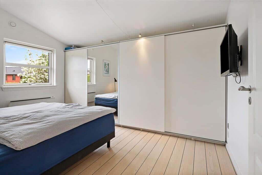 Schlafzimmer mit Bett, Kleiderschrank und Fenster mit Blick nach draußen.
