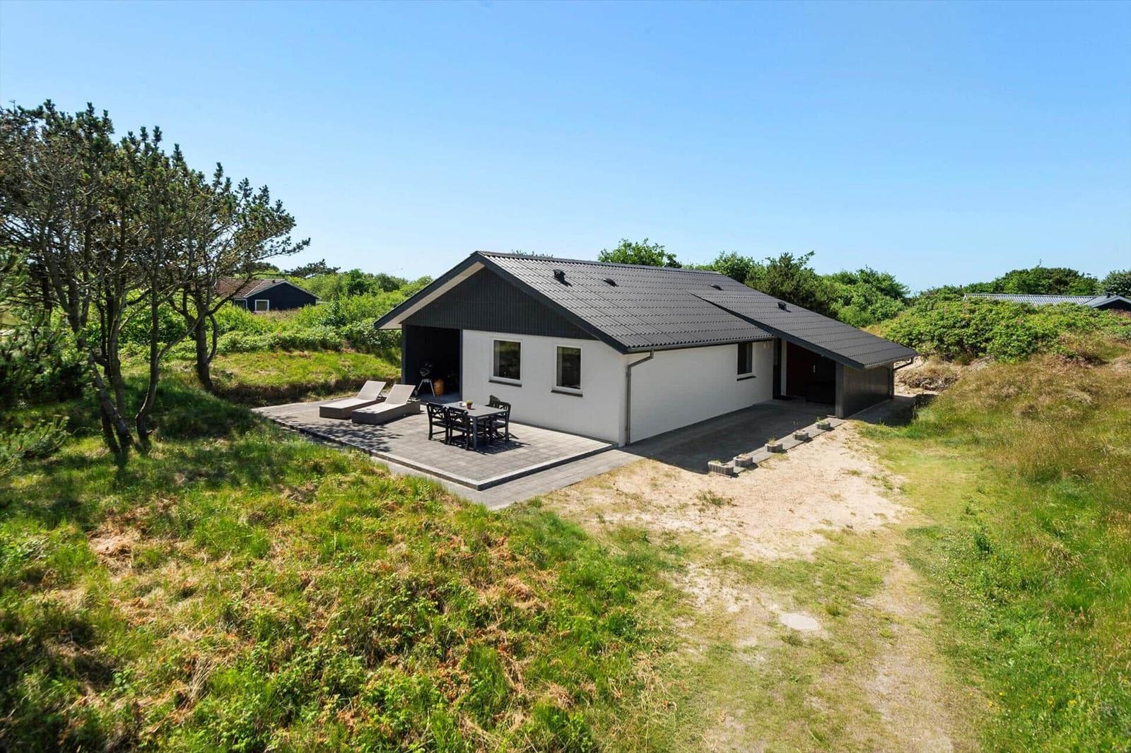 Moderne Villa mit Terrasse, Liegen und Tisch im Grünen.