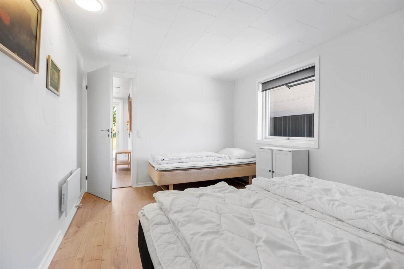 Schlafzimmer mit zwei Betten, Holzboden und Fenster. Tür führt in einen Flur.