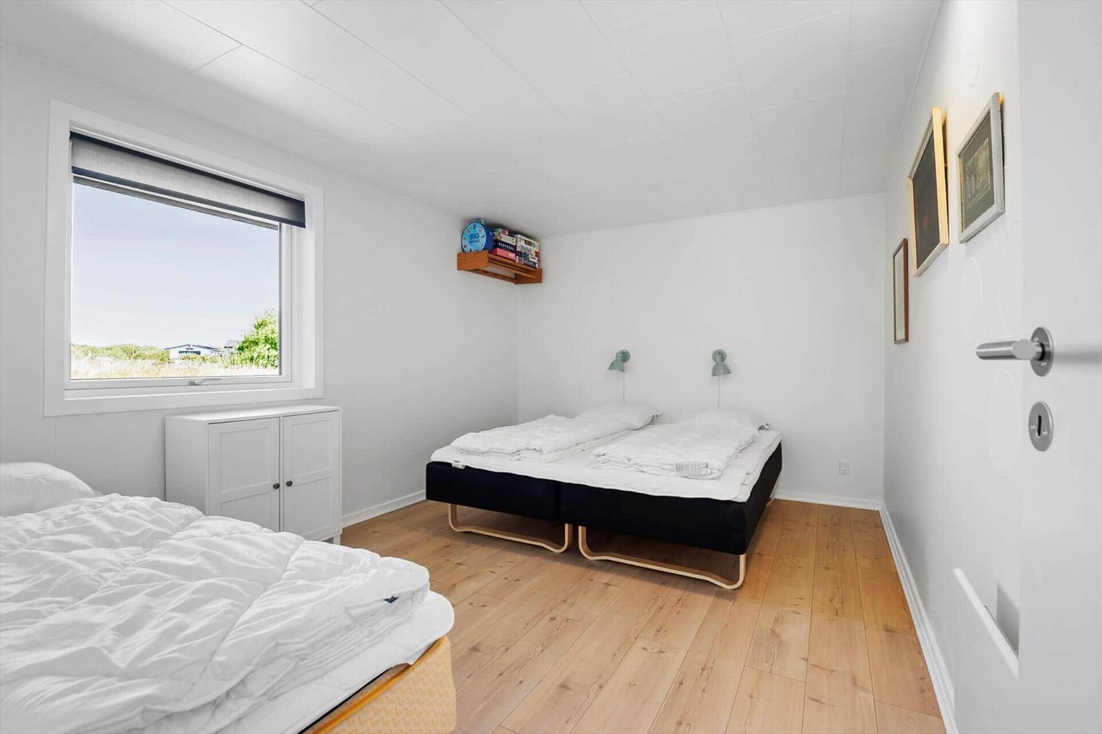 Schlafzimmer mit zwei Betten, Holzboden und Fenster mit Blick nach draußen.