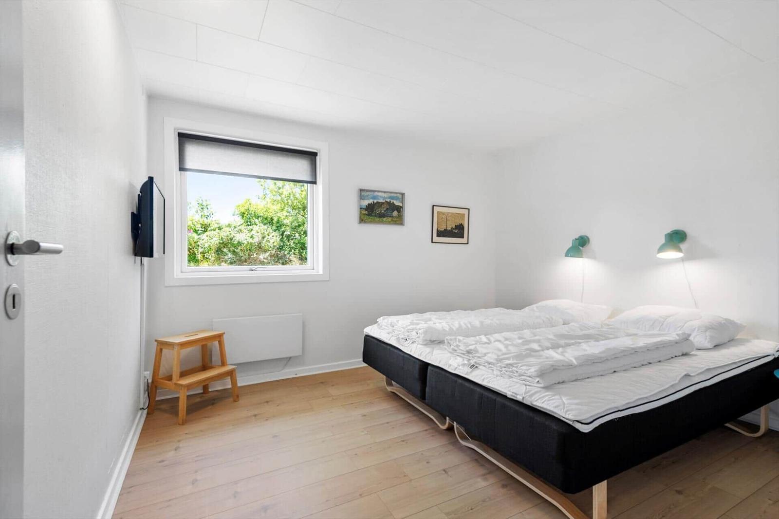 Ein Schlafzimmer mit Bett, Fenster, Wandlampen und Holzboden.