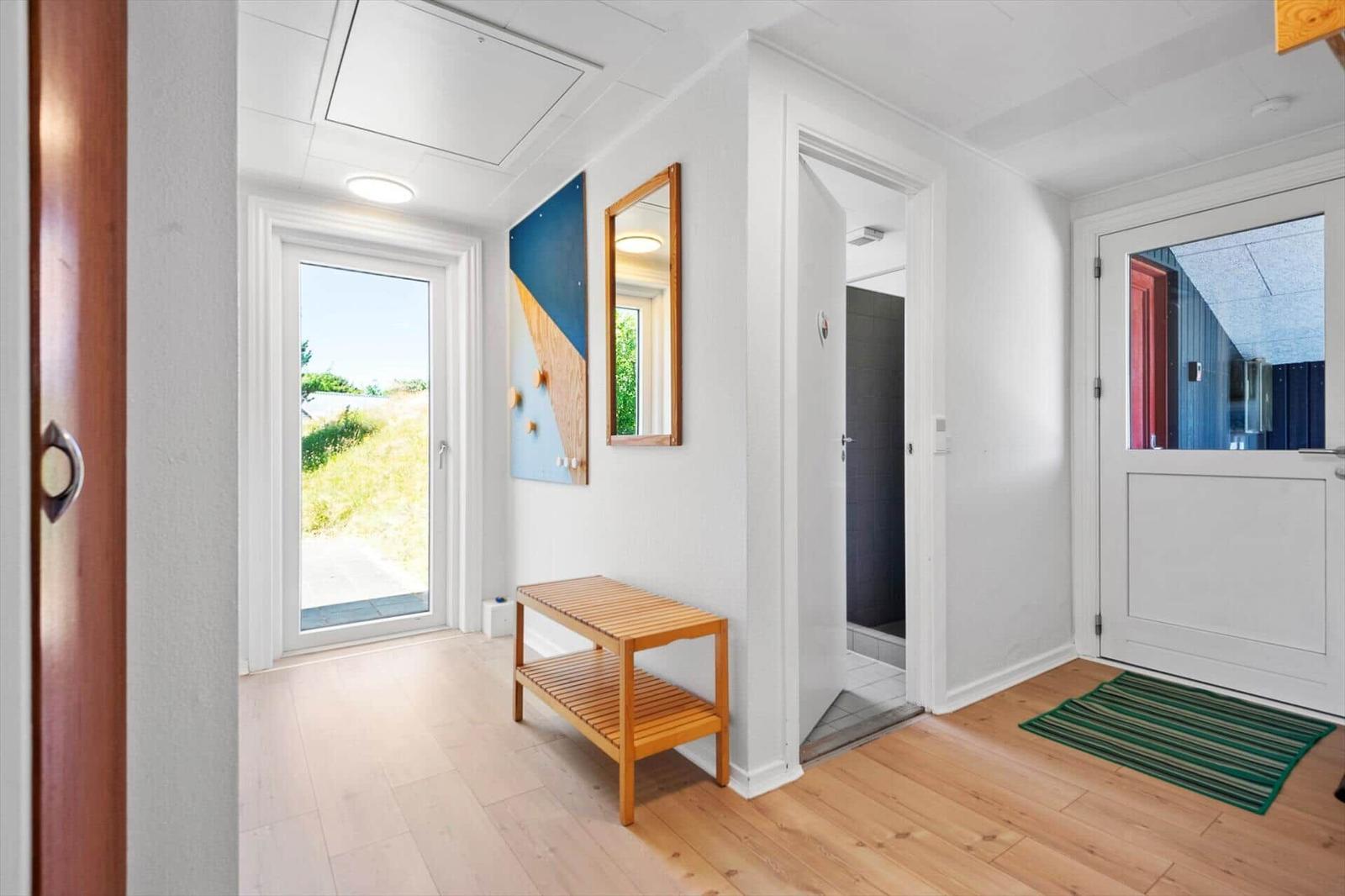 Eingangsbereich mit Holzbank, Spiegel und Fenster zur Außenterrasse.