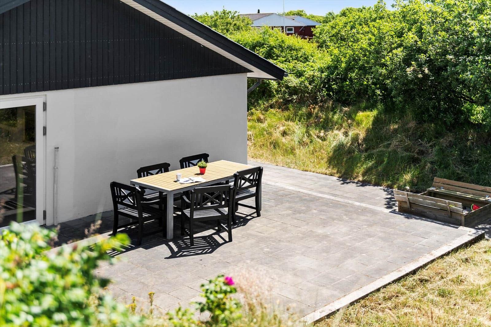 Terrasse mit Tisch und Stühlen neben einem Haus mit schwarzem Dach.