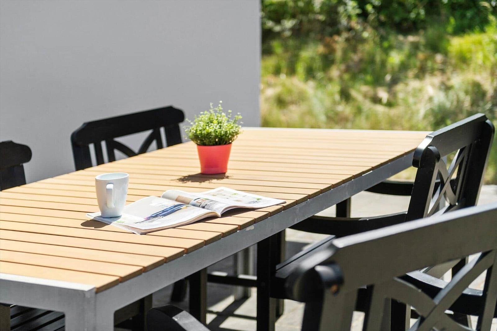 Helle Terrasse mit Tisch, Stühlen, Tasse und Zeitschrift. Ein kleiner Topf mit Pflanze.