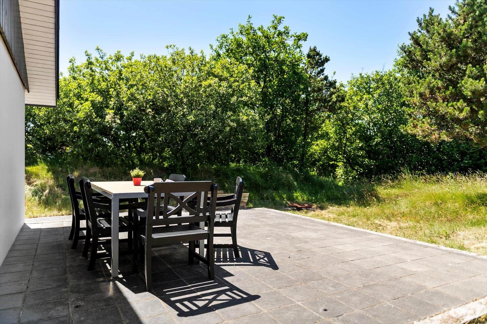 Terrasse mit Tisch und Stühlen, umgeben von Grün und Bäumen.