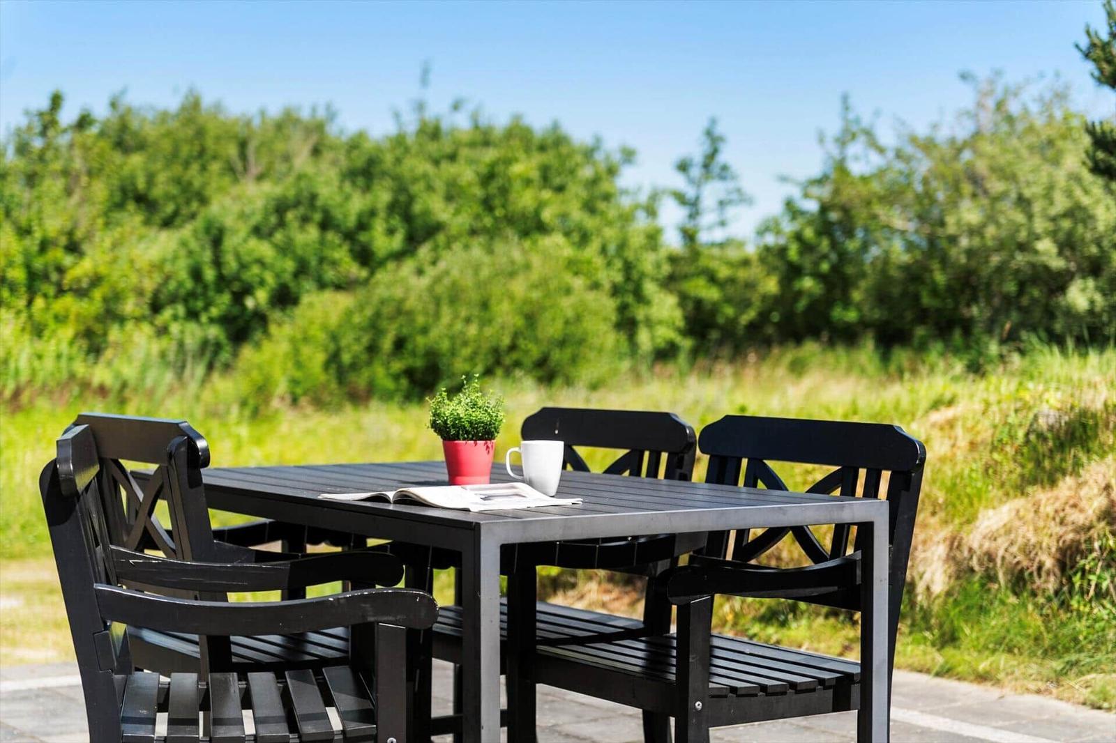 Schwarzer Garten-Tisch mit vier Stühlen, Tasse und Pflanze vor grünem Hintergrund.