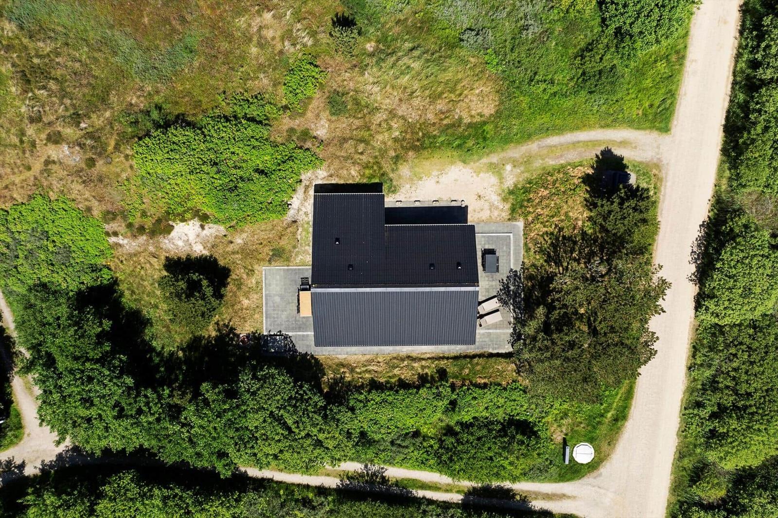 Moderne Villa mit dunklem Dach, umgeben von Grünflächen und Wald.