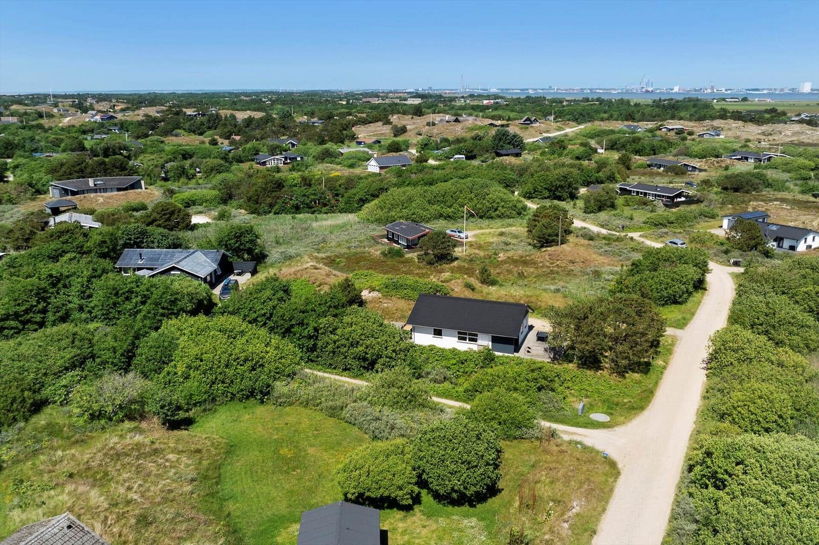 Aerial view of holiday homes among greenery with distant waterfront and industrial area.