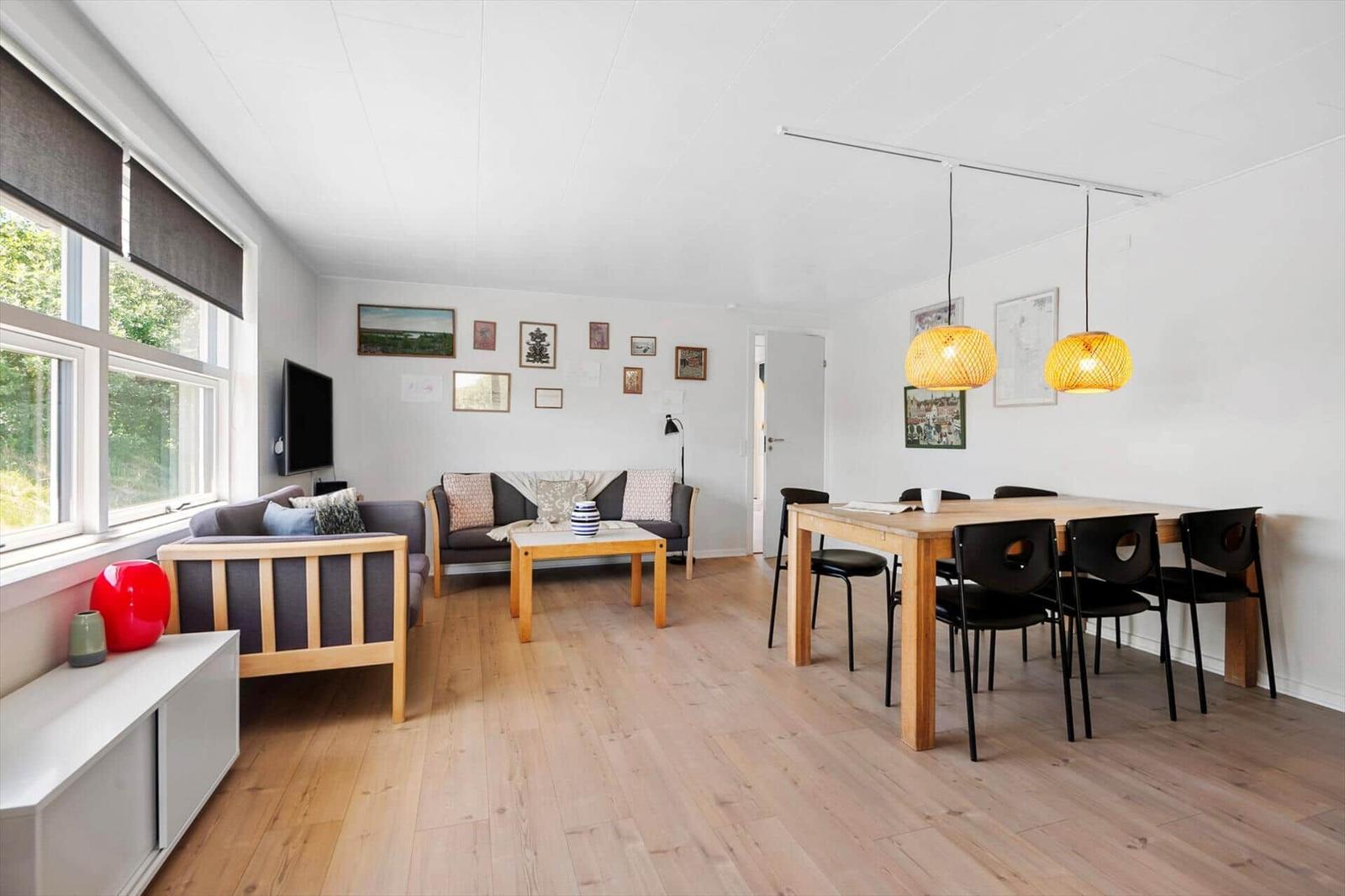 Wohn- und Essbereich mit Holzboden, Sofa, Esstisch und zwei Hängelampen.