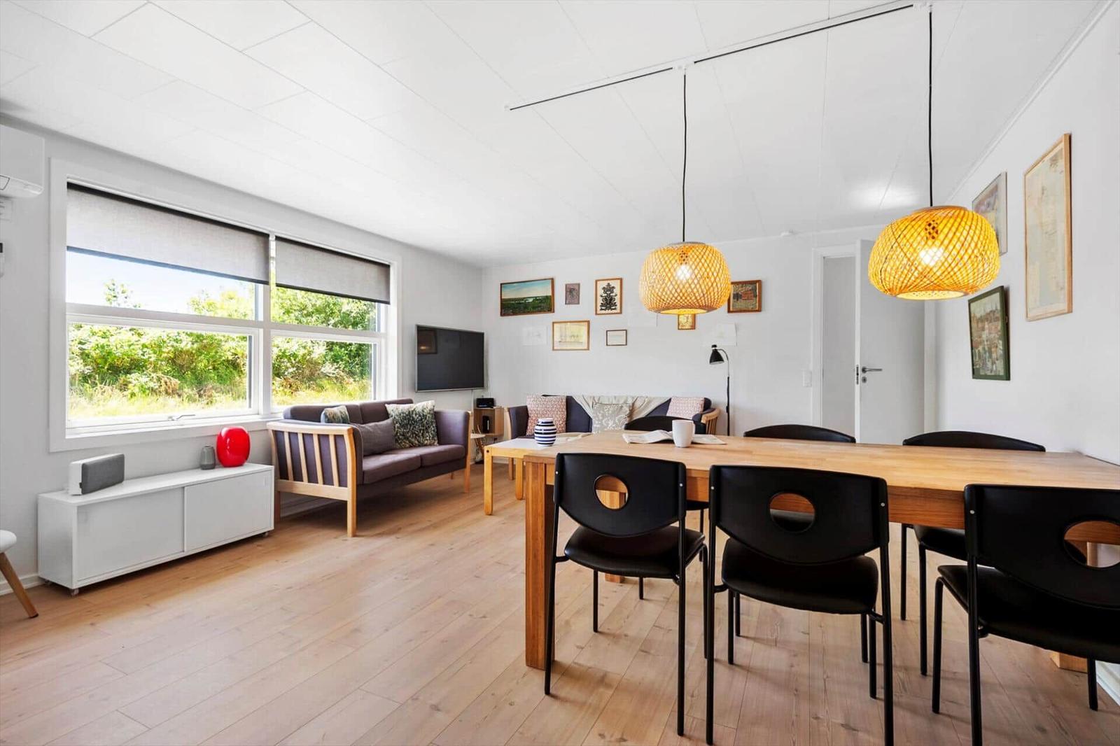 Wohn- und Essbereich mit Holzboden, Sofa, Esstisch und hängenden Lampen.