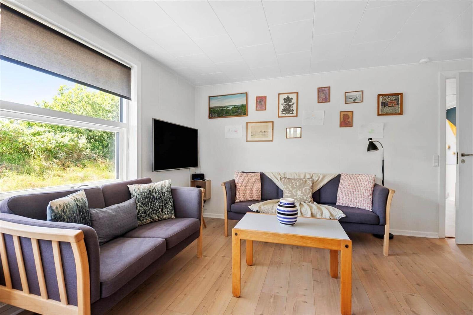 Wohnzimmer mit zwei Sofas, Holztisch und Wandbildern. Fenster mit Blick auf Grün.
