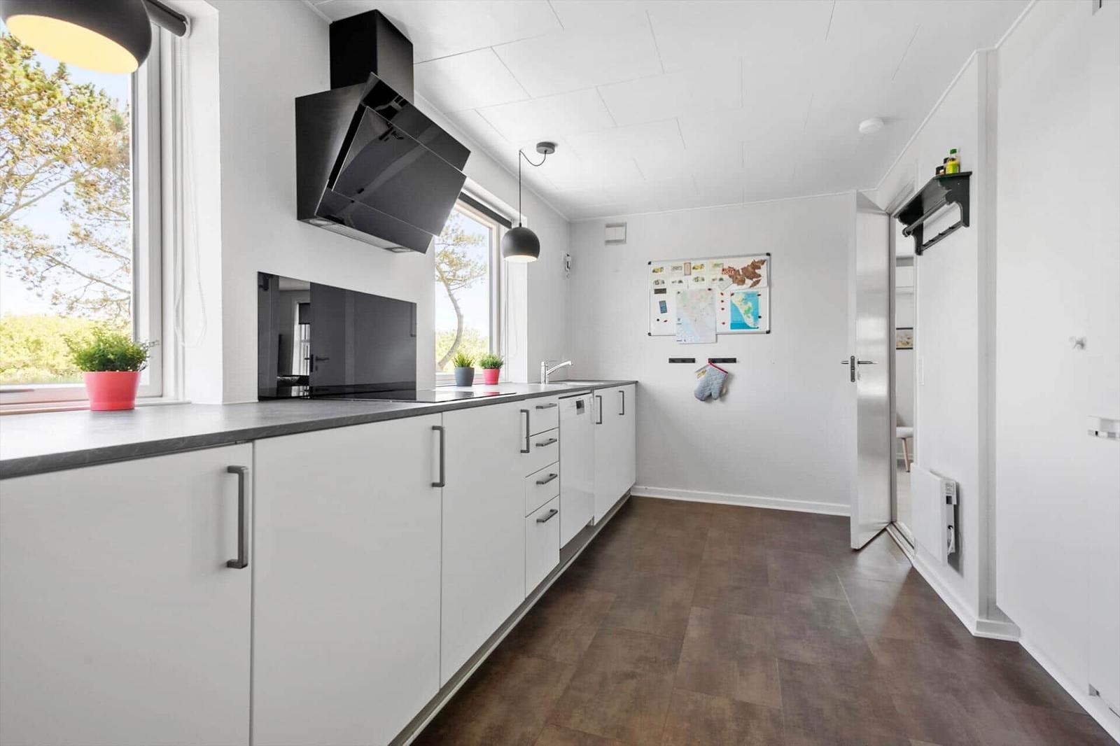 Moderne Küche mit weißen Schränken, schwarzer Arbeitsplatte und Fenstern mit Blick auf Bäume.