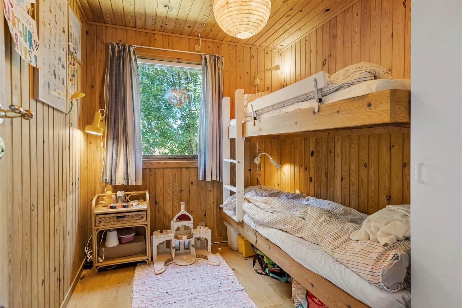 Ein Schlafzimmer mit Doppelstockbett, Holzwänden und einem Fenster mit Blick auf Bäume.