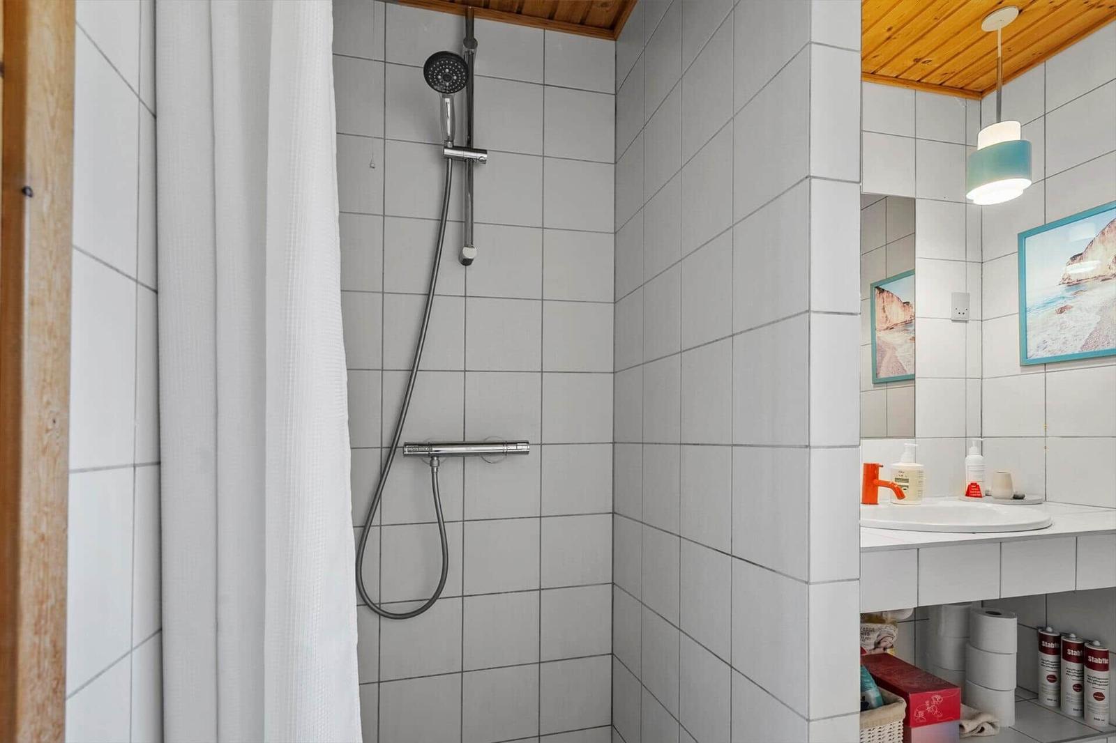 Badezimmer mit Dusche, Waschbecken und Spiegel. Holzdecke und weiße Fliesen.