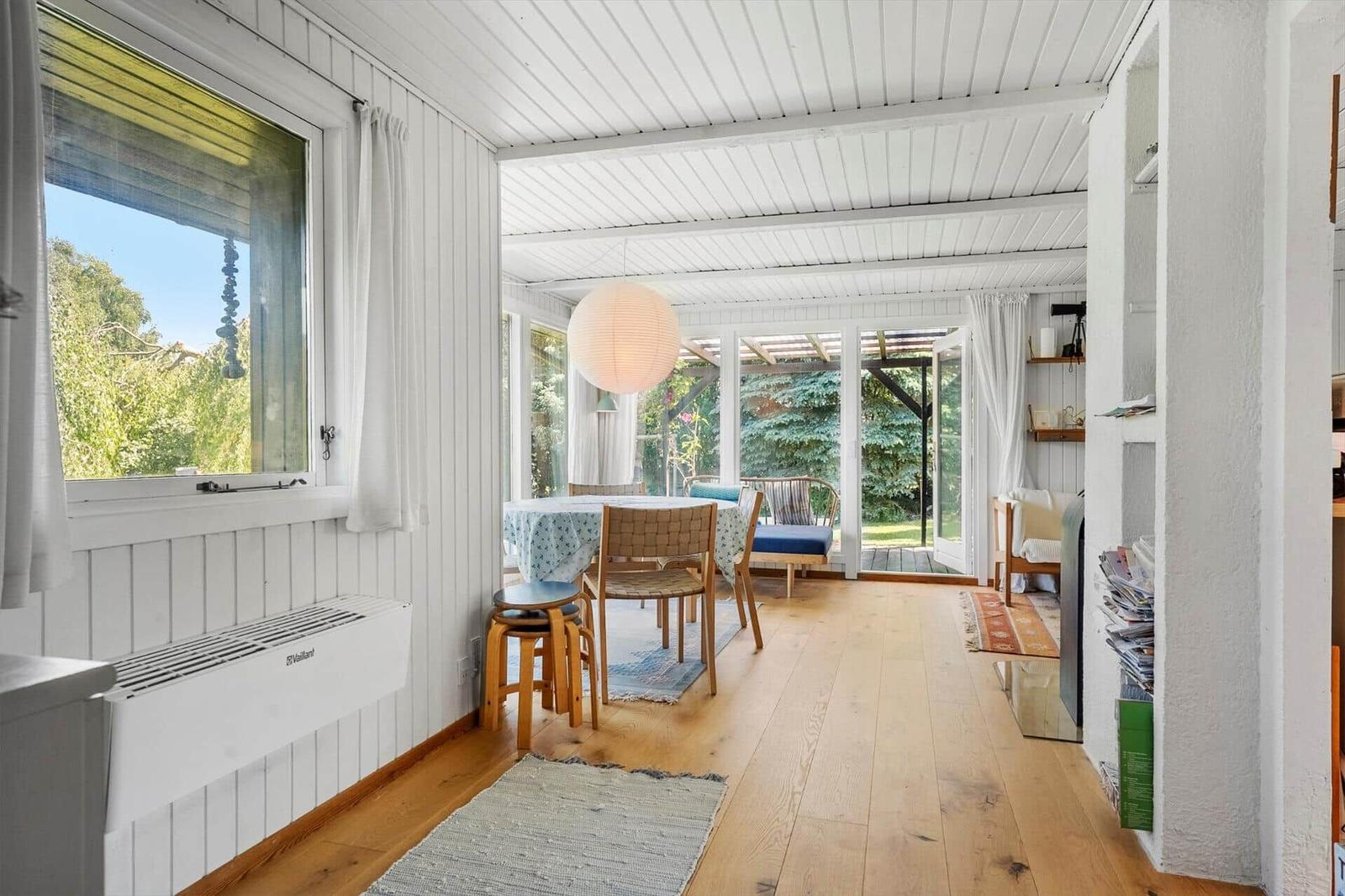 Wohnraum mit Holzboden, Tisch, Stühlen und Blick auf Garten.