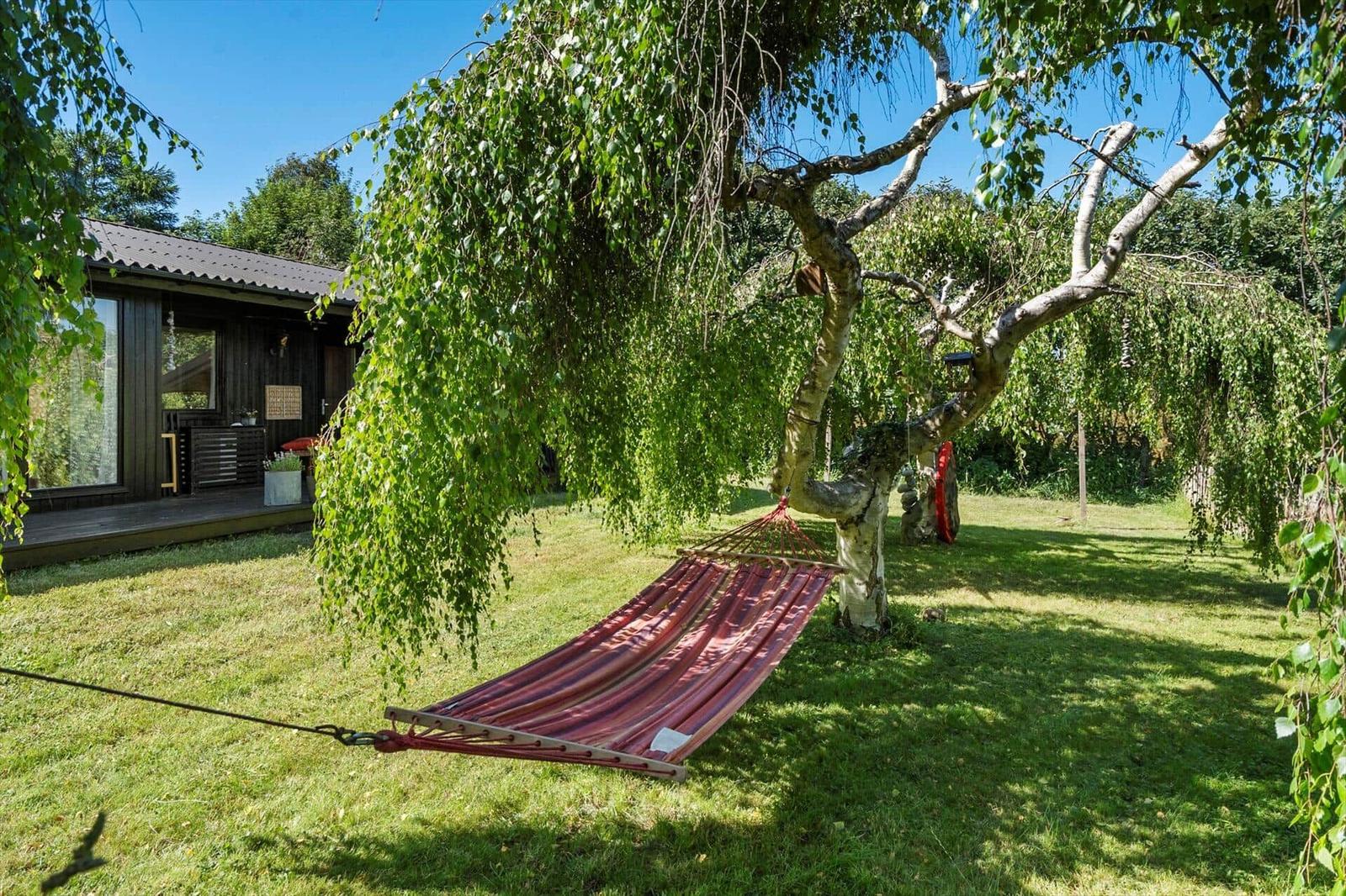 Roter Hängemattenschlafplatz unter einem Birnbaum im Garten neben einem Holzhaus.