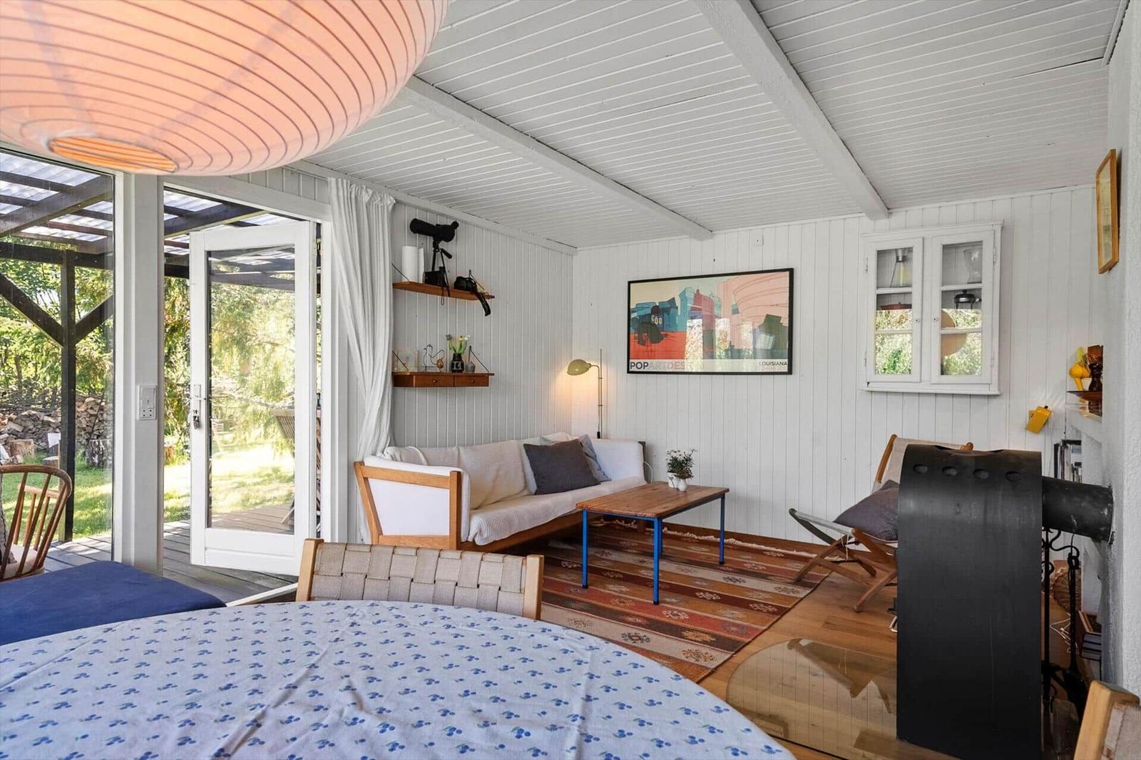 Wohnraum mit Sofa, Tisch und Blick auf Garten. Holzboden und weiße Wände.