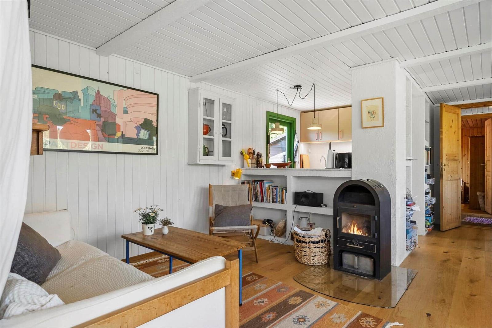 Wohnzimmer mit Kamin, Sofa, Tisch und Küchenbereich im Hintergrund.
