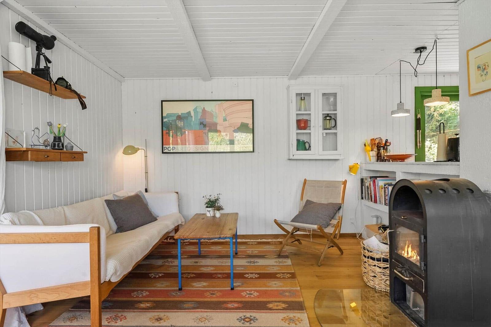 Wohnraum mit Sofa, Stuhl, Kamin und Wandbild. Holzboden und weiße Wände.