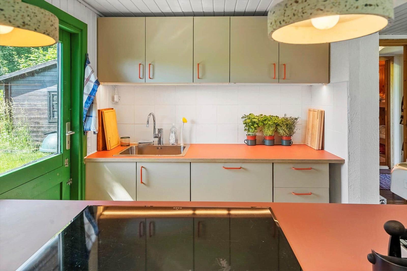 Küche mit orangefarbenem Arbeitsplatz, hellen Schränken und Pflanzen auf der Arbeitsfläche.