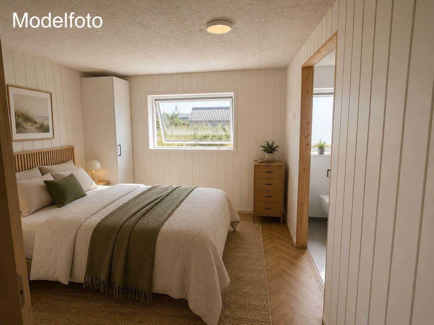 Schlafzimmer mit Bett, Kleiderschrank und Fenster. Holzfußboden und Türöffnung zum Badezimmer.
