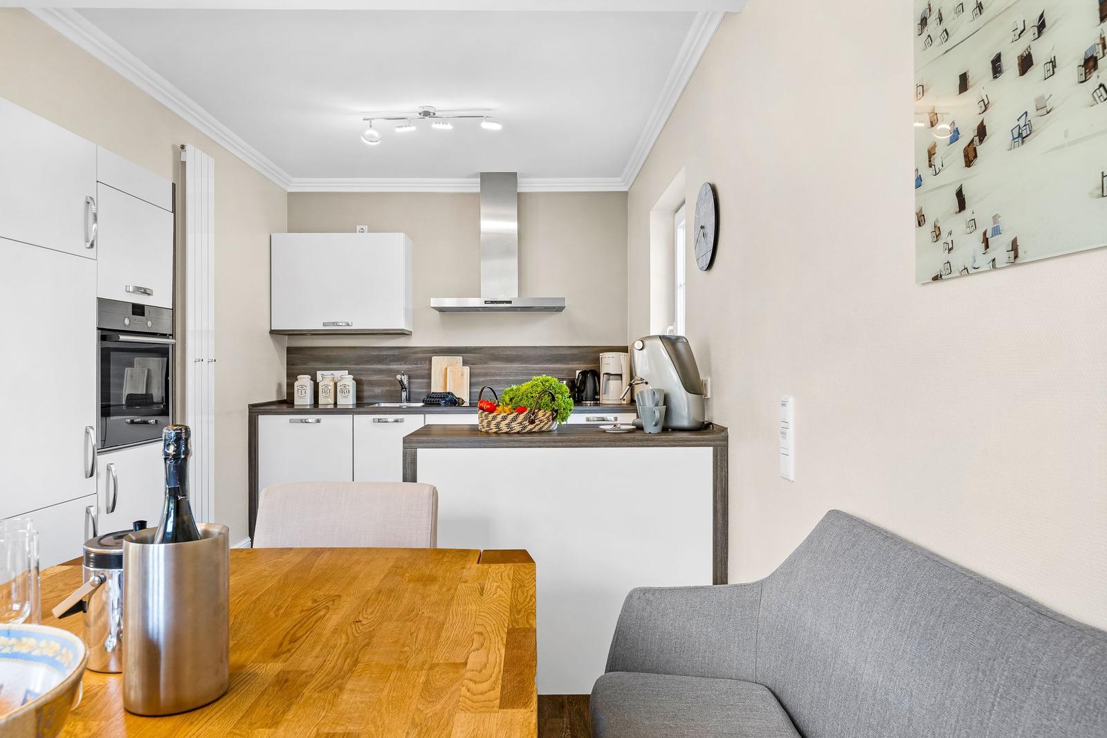 Kitchen with dining area and gray sofa. Wooden table, refrigerator, stove, and coffee machine.