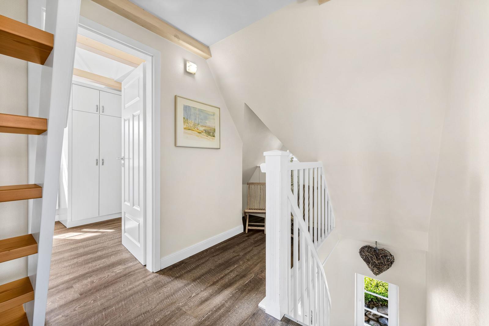 Staircase with wooden steps, white railings, and view into bedroom.